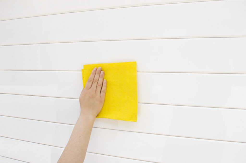 A homeowner cleaning her white garage door with a yellow cloth